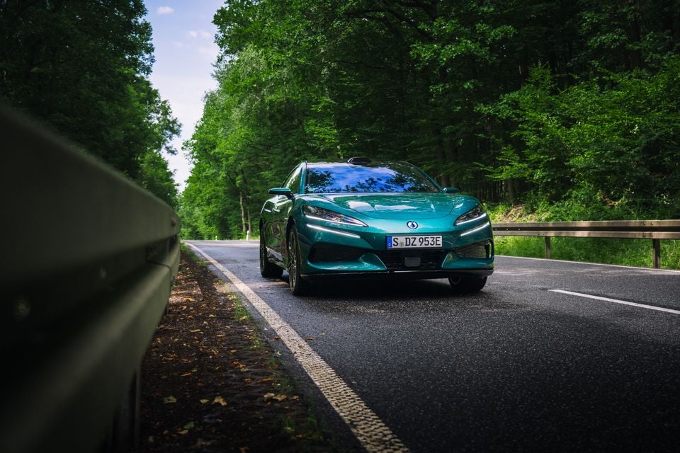 A teal Denza Z9 GT driving on a tree-lined road, seen from the front