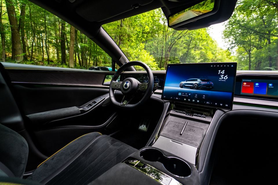 Interior of a Denza Z9 GT showing the steering wheel, large central touchscreen infotainment display, digital instrument cluster, and centre console with wireless charging pad
