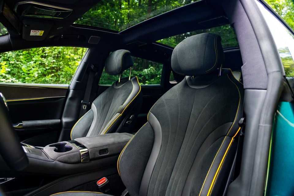 Dark grey suede-style front seats with yellow contrast stitching and a centre console armrest inside a Denza Z9 GT, with a panoramic sunroof visible above