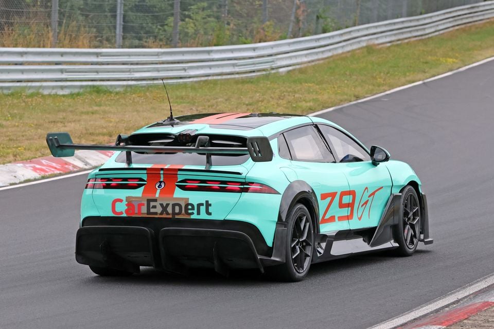 A Denza Z9 GT in a teal and orange race livery seen from the rear three-quarter angle on a racetrack, featuring a large rear wing and aggressive aerodynamic bodywork.
