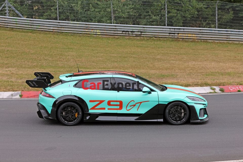 A teal and black Denza Z9 GT with large rear wing and racing livery seen from the side at a racing circuit
