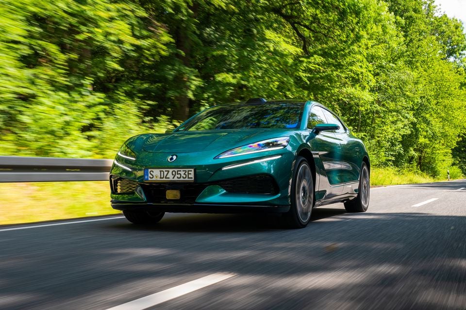 A teal Denza Z9 GT driving along a tree-lined road, seen from the front