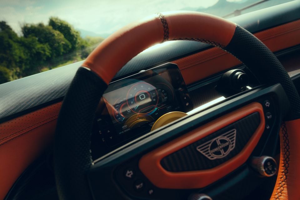 Close-up of the Donkervoort P24 RS steering wheel and digital instrument cluster, featuring orange leather trim and carbon fibre accents