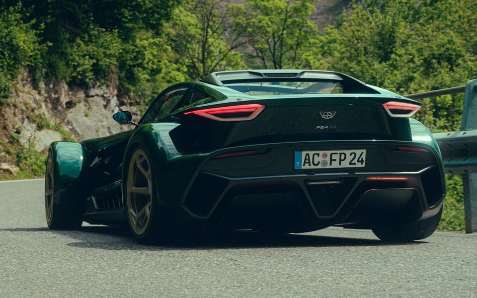 A dark green Donkervoort P24 RS supercar seen from the rear on a mountain road, with carbon fibre bodywork and gold alloy wheels