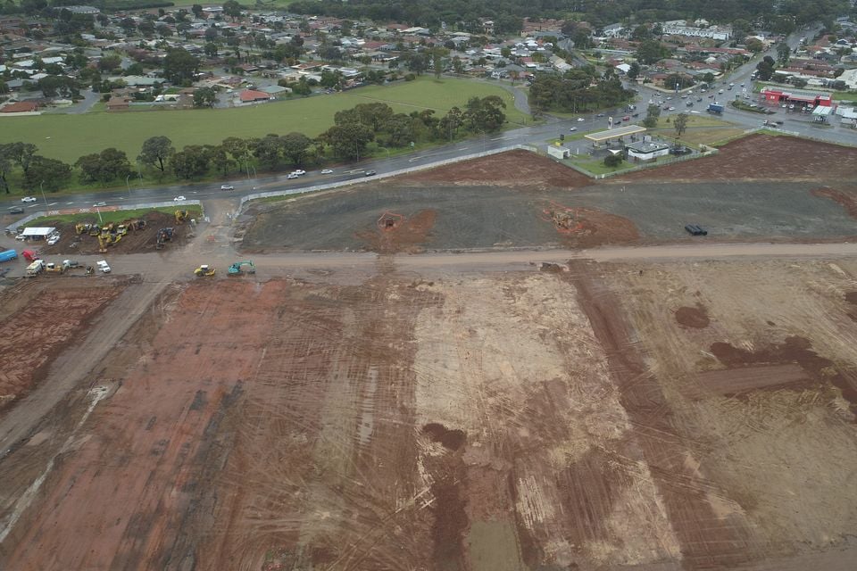 Aerial drone view of a large cleared construction site in a suburban Australian area, with excavation machinery visible and residential streets in the background.