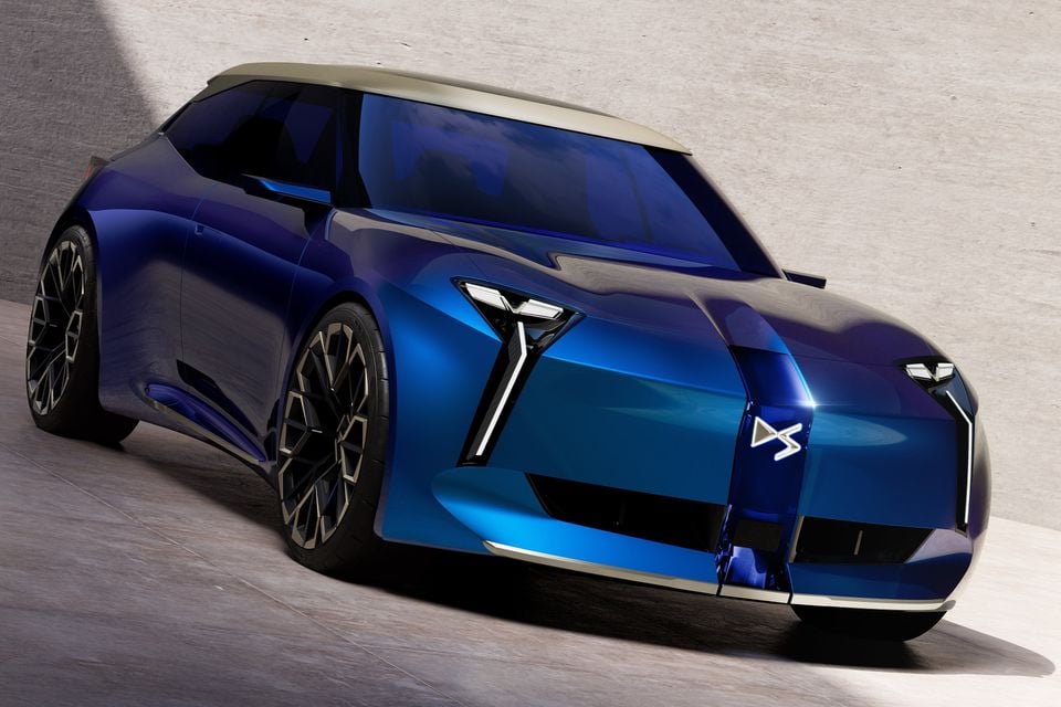 A blue DS concept hatchback with a gold roof and slim vertical headlights, seen from the front three-quarter angle against a concrete wall