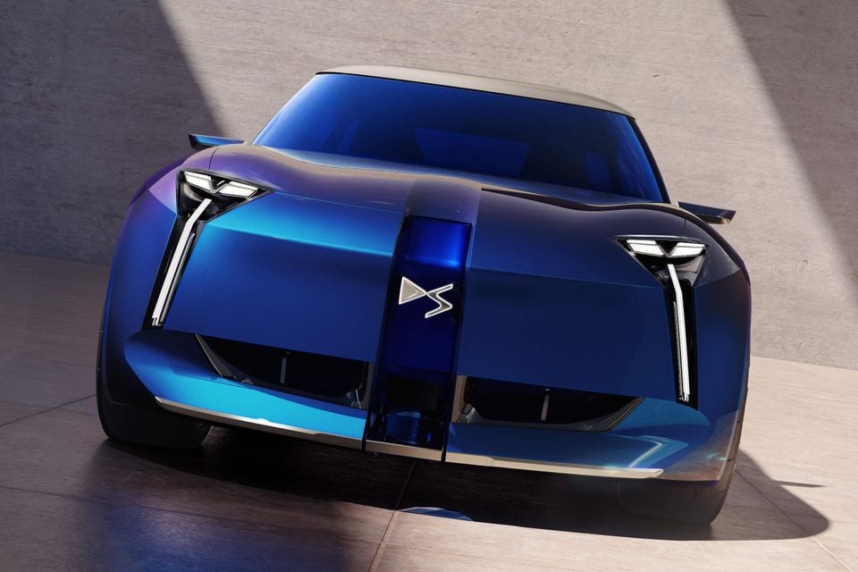 Um carro-conceito DS azul com assinaturas de luz LED verticais e um emblema DS central, visto de frente em uma sala de concreto iluminada pelo sol