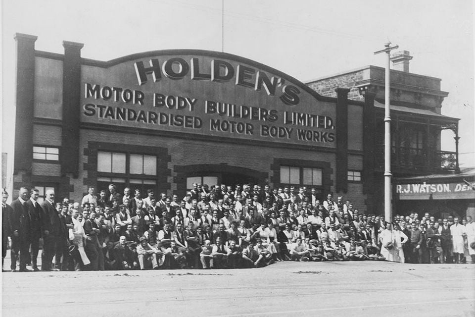 A black-and-white historical photograph of the Holden's Motor Body Builders Limited Standardised Motor Body Works building, with a large group of workers posing out front.