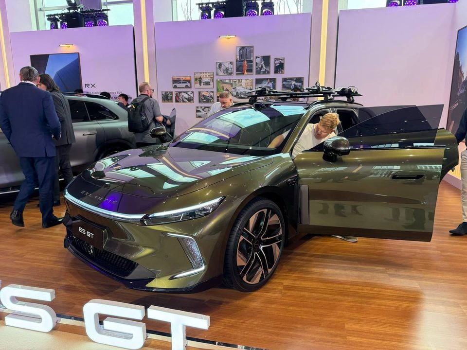 Green Exlantix ES GT shooting brake seen from the front three-quarter angle with a front door open and a visitor inspecting the cabin.
