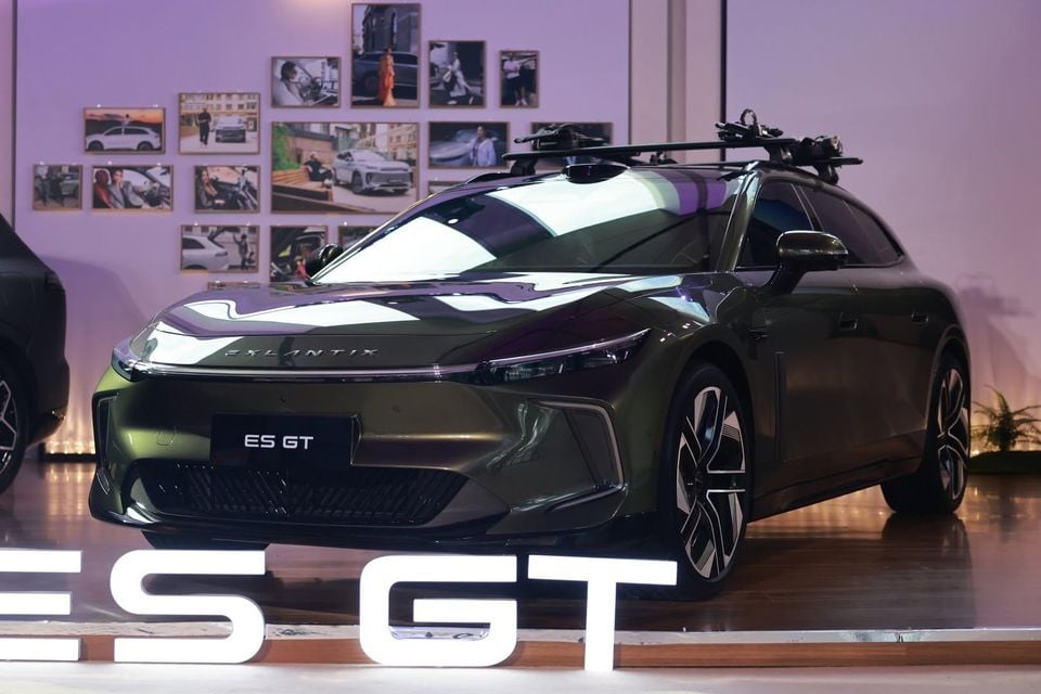 A dark green Exlantix ES GT wagon with roof-mounted bike racks displayed at a launch event, seen from the front left