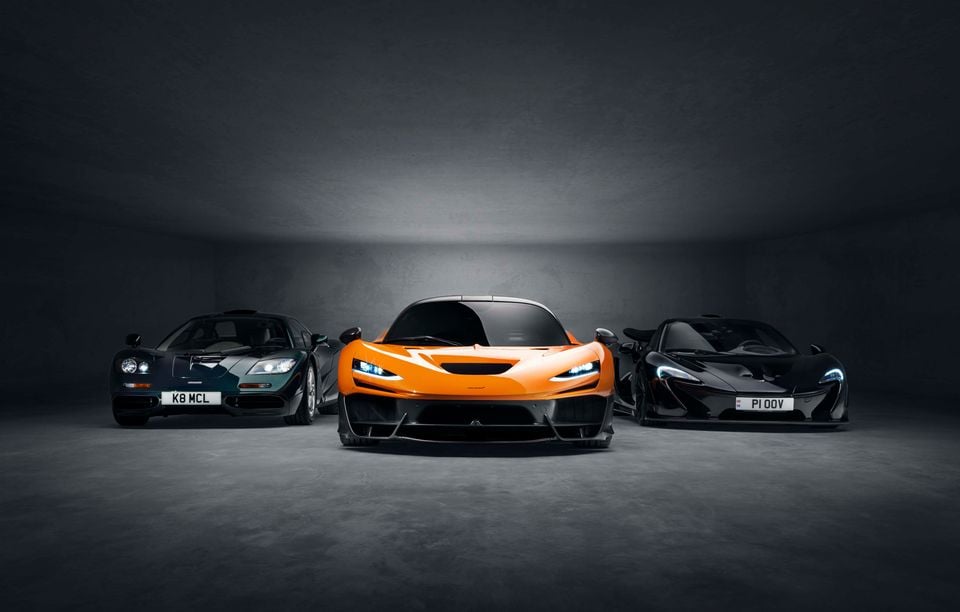 Three McLaren supercars — the F1, P1, and W1 — photographed together in a dark studio setting, with the orange W1 front and centre