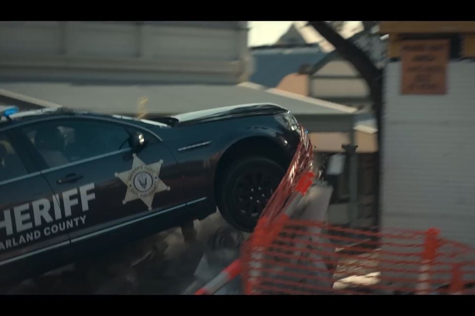 A black Holden Caprice Sheriff's deputy police car crashing through a barrier during what appears to be a film or TV production stunt