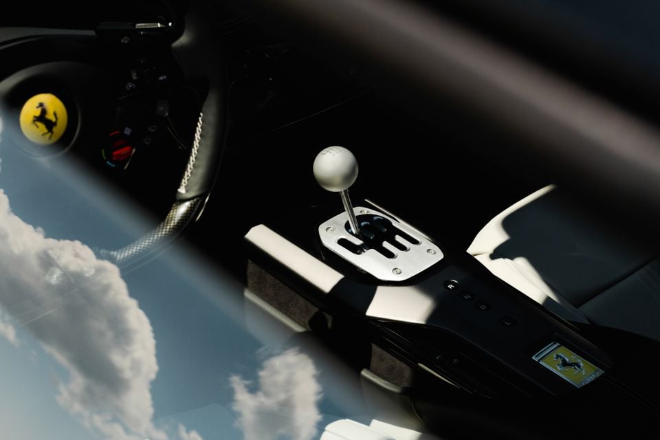Ferrari 12Cilindri interior showing a manual gearshift with a white ball-shaped gear knob, metal gate surround, and the Ferrari prancing horse badge visible, with the steering wheel in the background