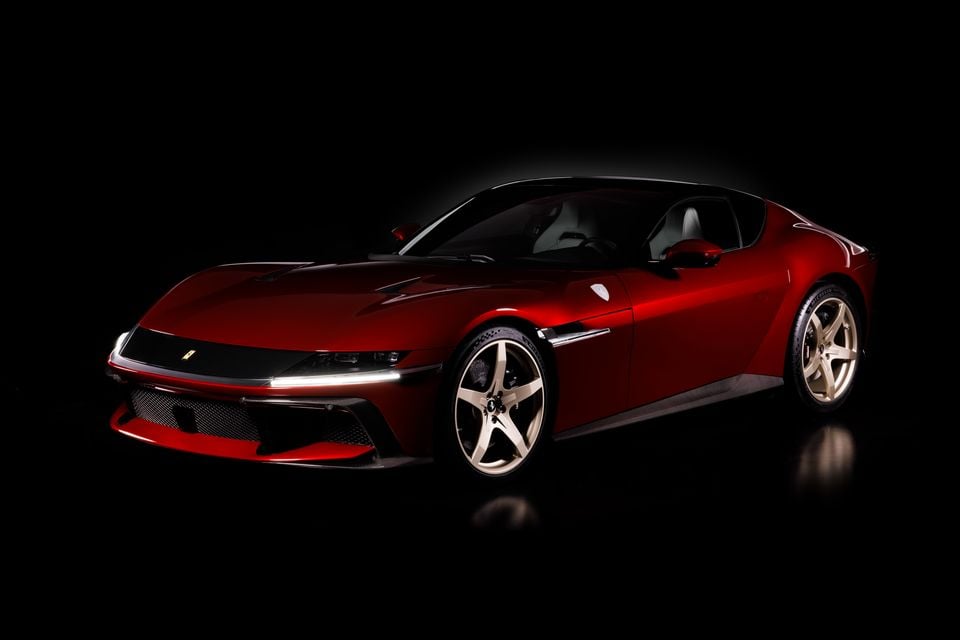 A red Ferrari 12Cilindri coupe photographed from a front three-quarter angle against a dark studio background.