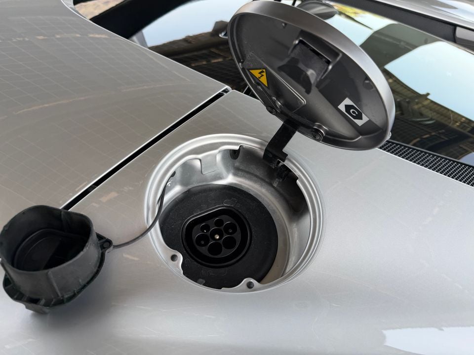 Close-up of an open electric vehicle charging port on a silver car, showing a Type 2 AC charge socket with the cover flipped open