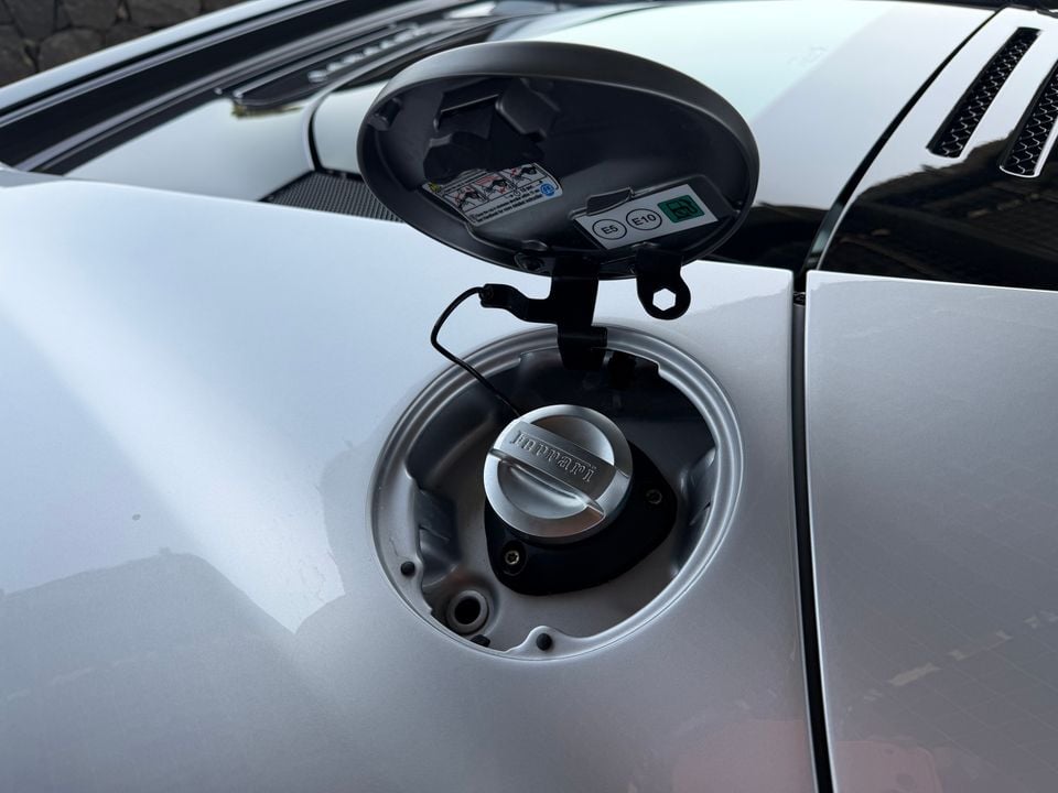 Close-up of an open fuel filler cap on a white Ferrari, showing the branded fuel cap and fuel type labels inside the flap