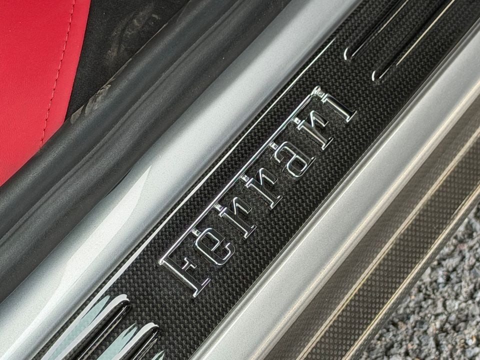 Ferrari door sill plate with chrome Ferrari lettering on a carbon fibre finish, with red leather interior visible above