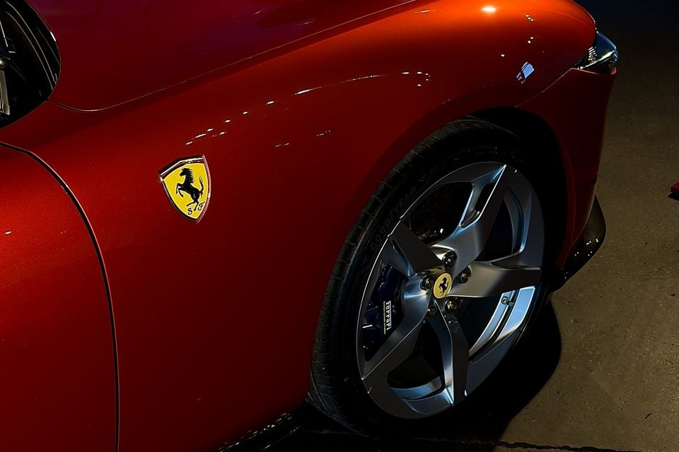 Close-up of a red Ferrari's front fender, showing the prancing horse badge and a five-spoke alloy wheel with blue brake calipers