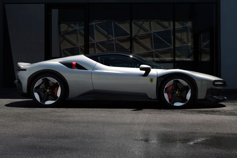 A silver Ferrari SF90 supercar seen from the side, parked outside a building