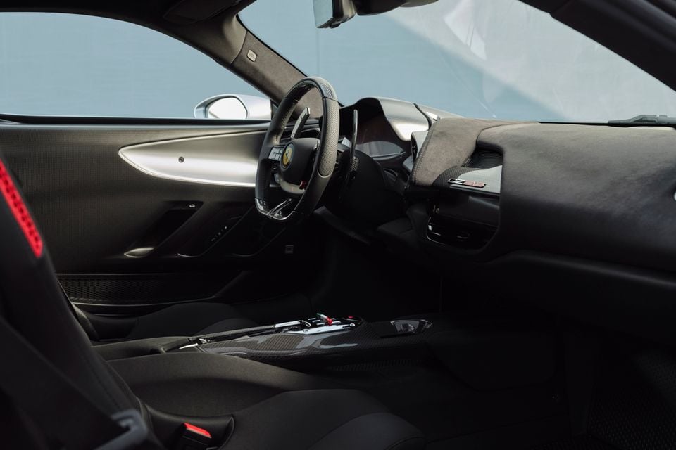 Ferrari interior showing the steering wheel with prancing horse badge, carbon fibre centre console, Alcantara dashboard trim, and sport seats viewed from the passenger side