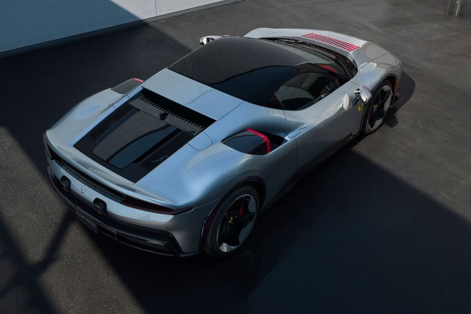A silver Ferrari F80 supercar seen from a high rear three-quarter angle, showing its sculpted bodywork, black roof, red interior accents, and large dark alloy wheels