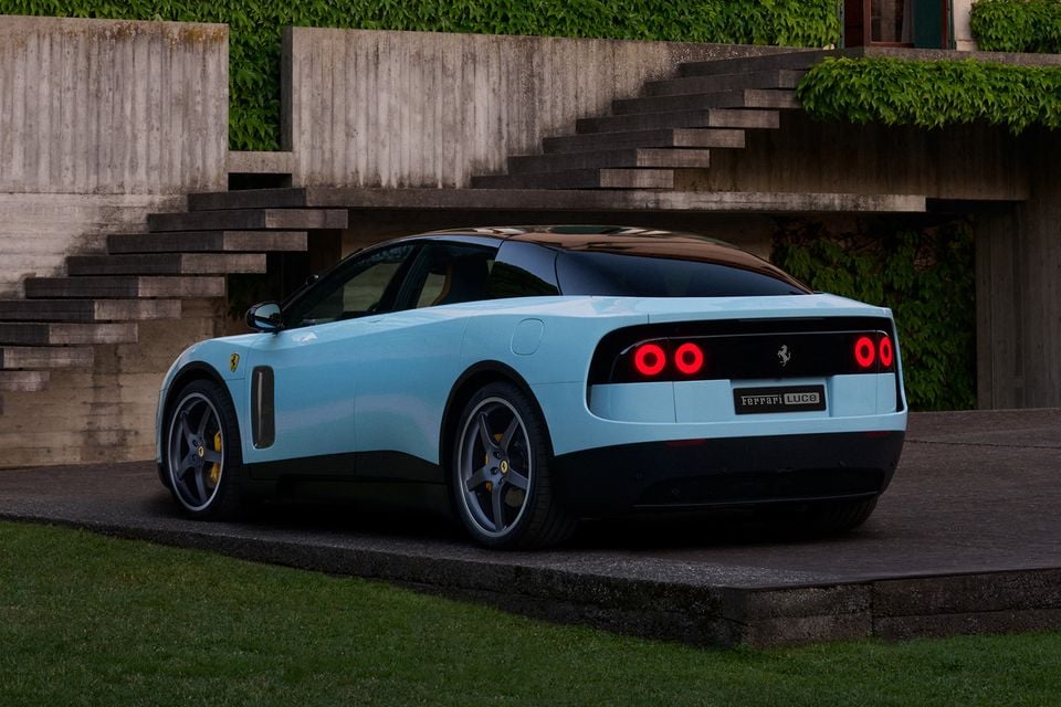 A light blue Ferrari Luce coupe seen from the rear three-quarter angle, parked on a raised platform in front of a concrete staircase with ivy-covered walls