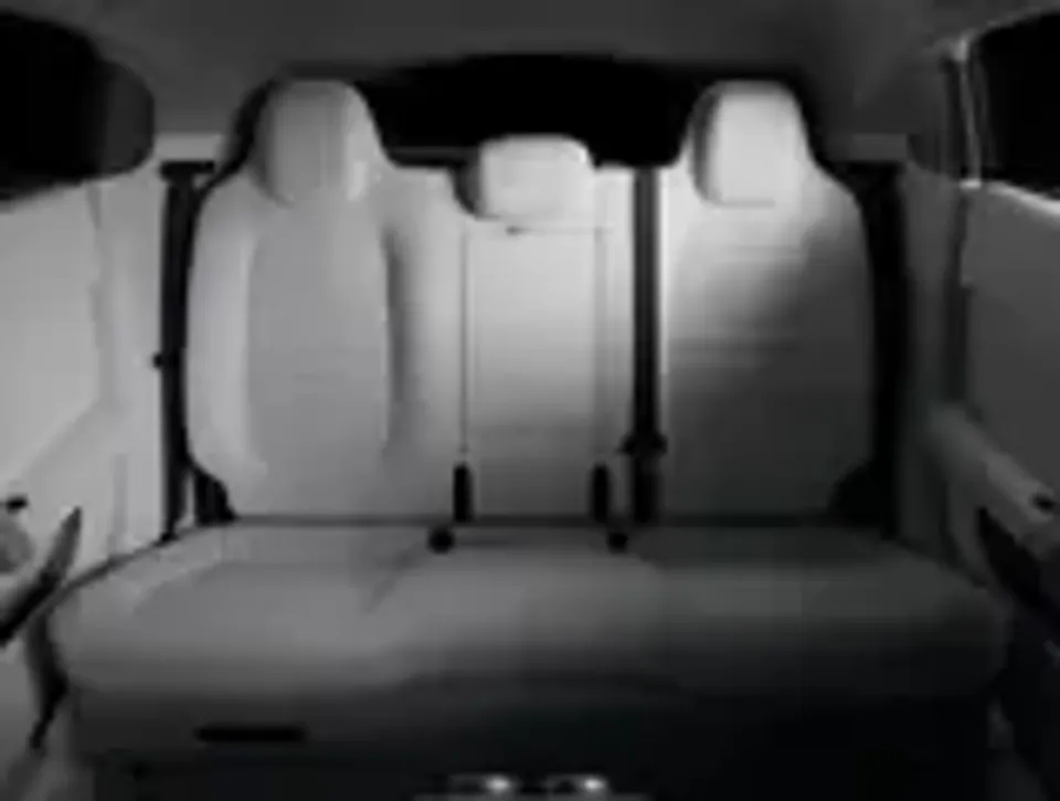 The rear passenger bench seat of a car interior, viewed from the boot area, showing light-coloured upholstery and three headrests.