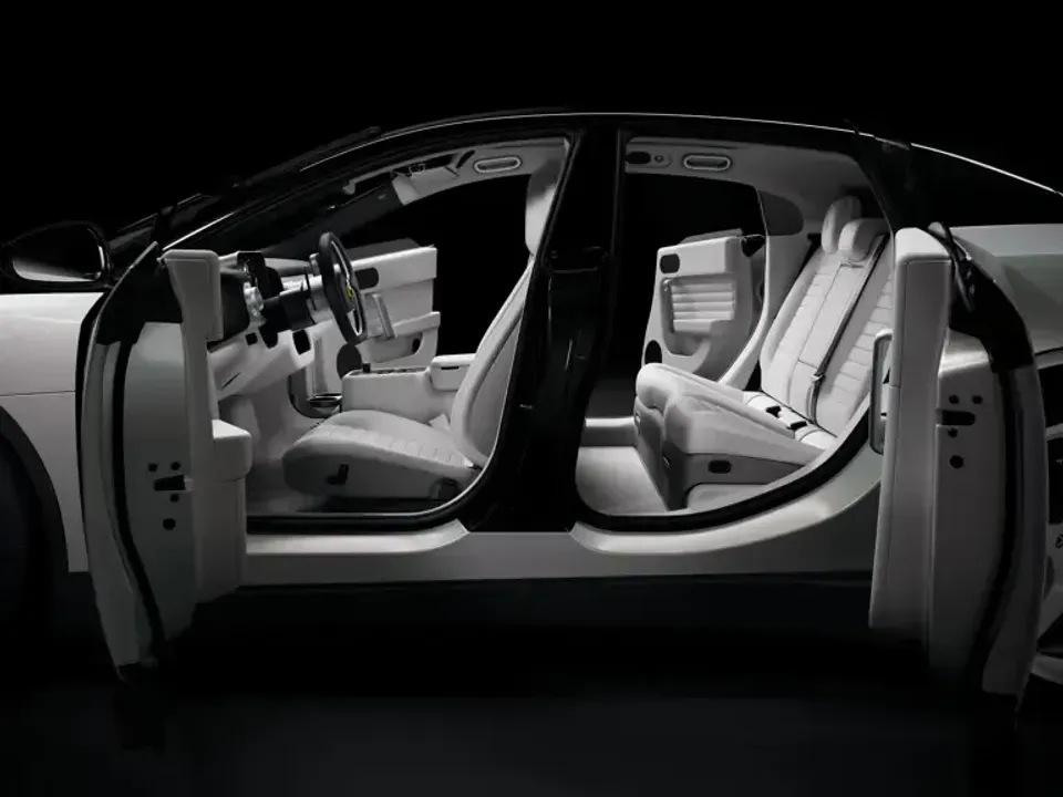 A Ferrari Luce with all four doors open, revealing a white leather interior with front and rear seats, viewed from the side against a dark background.