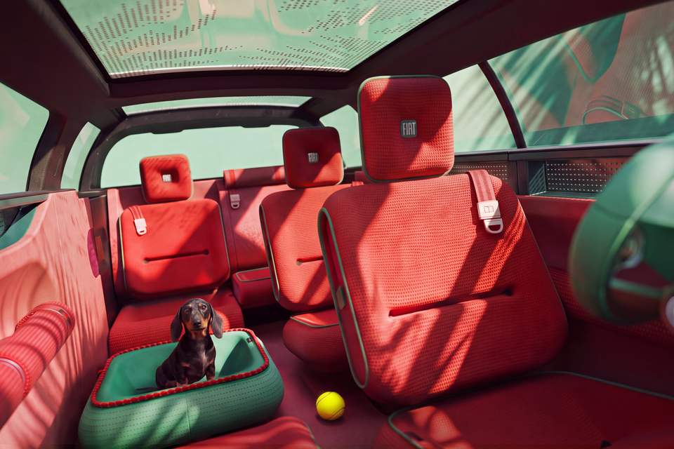 Interior of the Fiat Multi-Play concept with red woven seats, a large glass roof and a dachshund sitting in a green pet bed beside a tennis ball