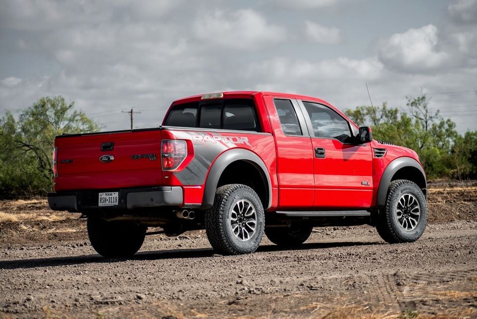 A red Ford F-150 SVT Raptor ute seen from the rear three-quarter angle on a dirt track in a rural setting