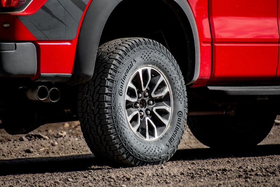 Close-up of a Continental CrossContact AT2 all-terrain tyre on a red Ford F-150 SVT Raptor, parked on a gravel surface