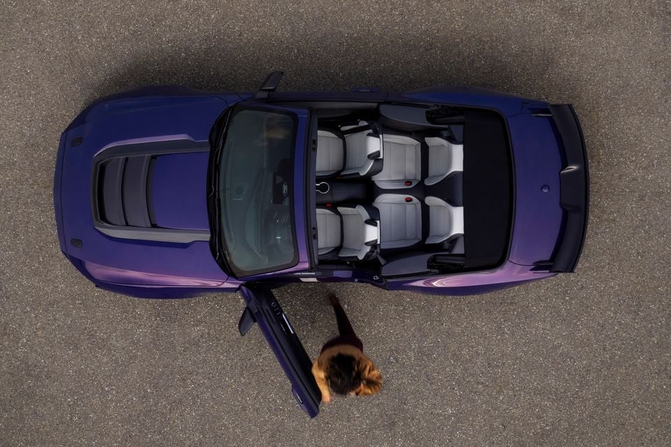 Overhead view of a purple Ford Mustang Dark Horse convertible with the roof down, showing the light grey interior and four seats, with a person standing beside the open door
