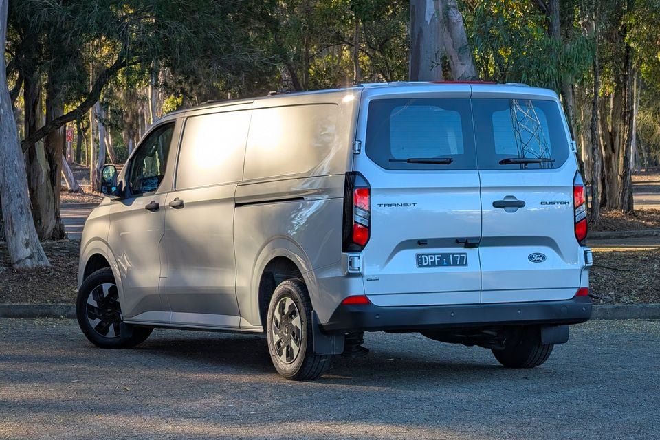 A white Ford Transit Custom PHEV van parked among trees, seen from the rear quarter