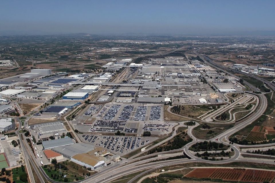 Aerial view of a large car manufacturing plant and vehicle storage yard, identified as the Ford factory in Valencia, Spain, surrounded by roads and industrial buildings