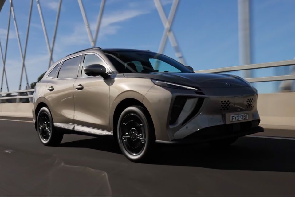 A gold/champagne Forthing Electric SUV driving across a bridge, seen from the front-side angle