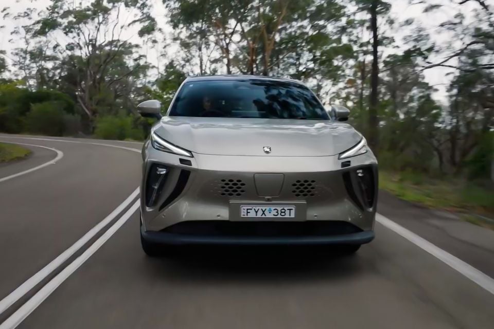 A silver Forthing electric SUV driving towards the camera on a winding Australian road lined with eucalyptus trees, seen from the front.