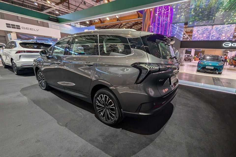A grey Forthing TK7 MPV seen from the rear three-quarter angle at a motor show, with Geely branding visible in the background