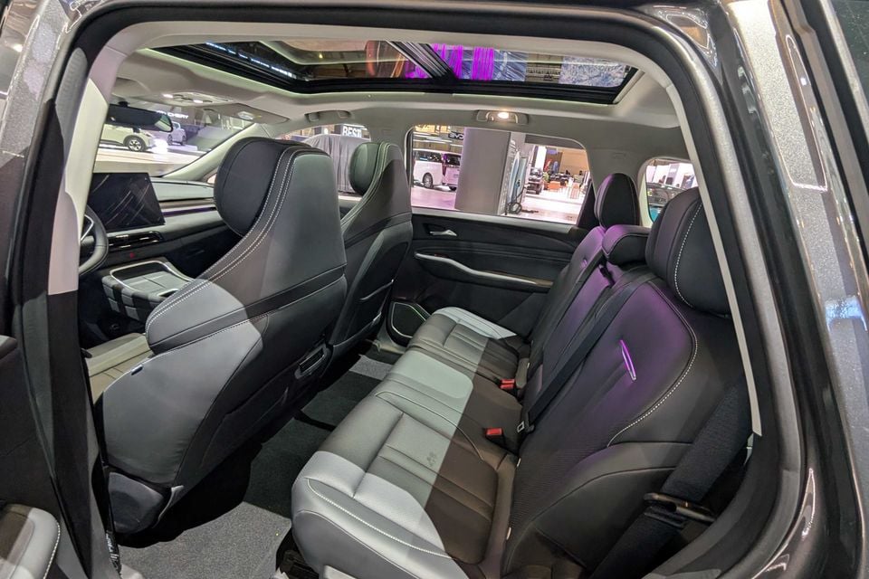 Interior view of a Forthing TK7 SUV showing two rows of black and grey leather seats, viewed through an open rear door at a motor show