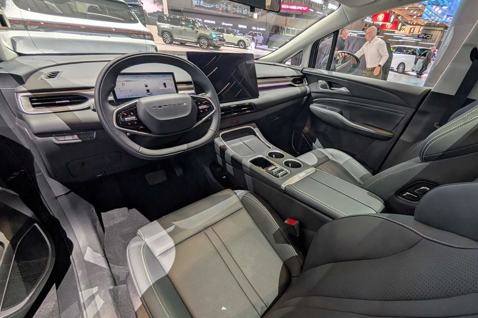 Interior of a Forthing TK7 showing the dashboard, large central touchscreen, steering wheel, centre console, and front seats, photographed at a motor show