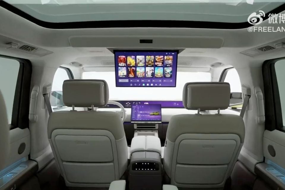 Interior rear cabin view of a Freelander 8 showing light grey leather seats, a large roof-mounted entertainment screen, and a central touchscreen display