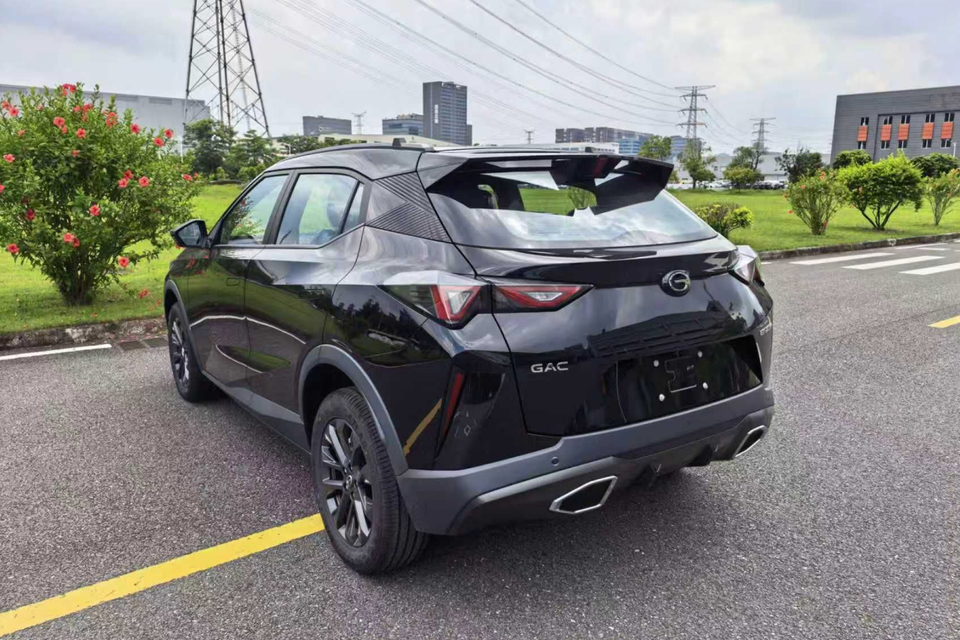 A black GAC Emzoom SUV seen from the rear three-quarter angle, parked in an urban area with greenery in the background