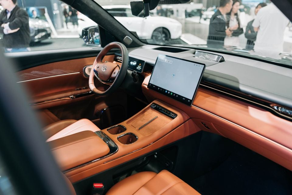 Interior of a GAC S7 showing tan leather seats, centre console, and a large touchscreen infotainment display, viewed from the passenger side at a motor show