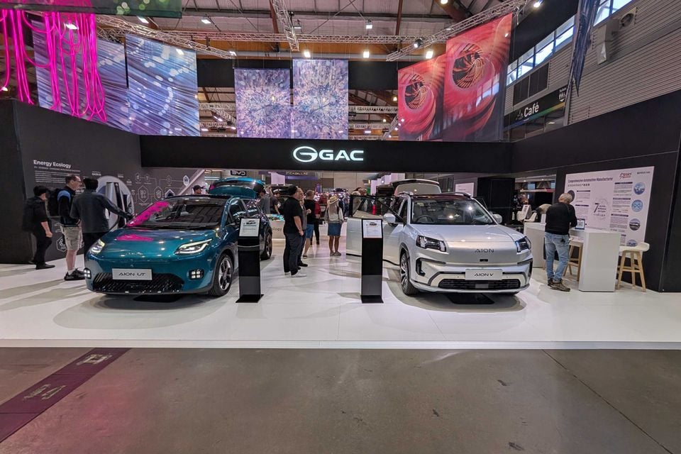 A teal GAC Aion UT and a white GAC Aion V SUV on display at a motor show, both shown at a front-quarter angle