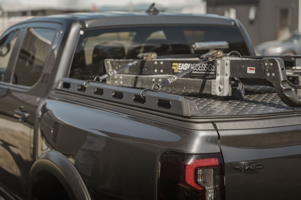 The tray bed of a dark grey GMC ute loaded with Easy Access Co. equipment secured with ratchet straps, seen from the rear quarter