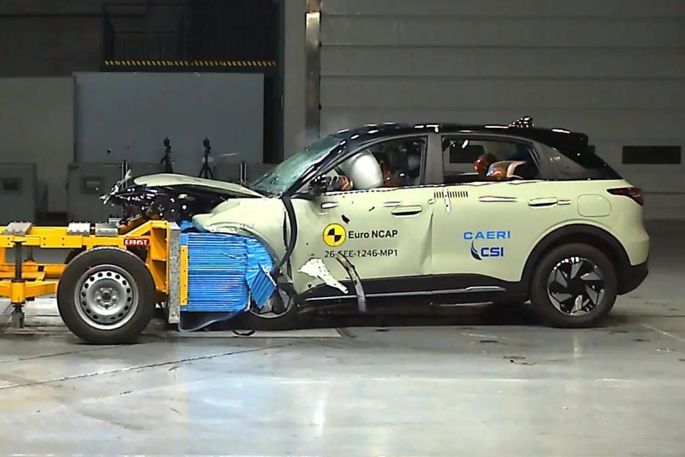 A Geely EX2 small SUV after a frontal offset crash test at a Euro NCAP facility, with its front end crushed against a blue deformable barrier.