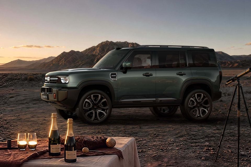 A dark green Geely Galaxy Cruiser SUV parked in a desert landscape at dusk, seen from the front-side, with champagne bottles and a telescope in the foreground.