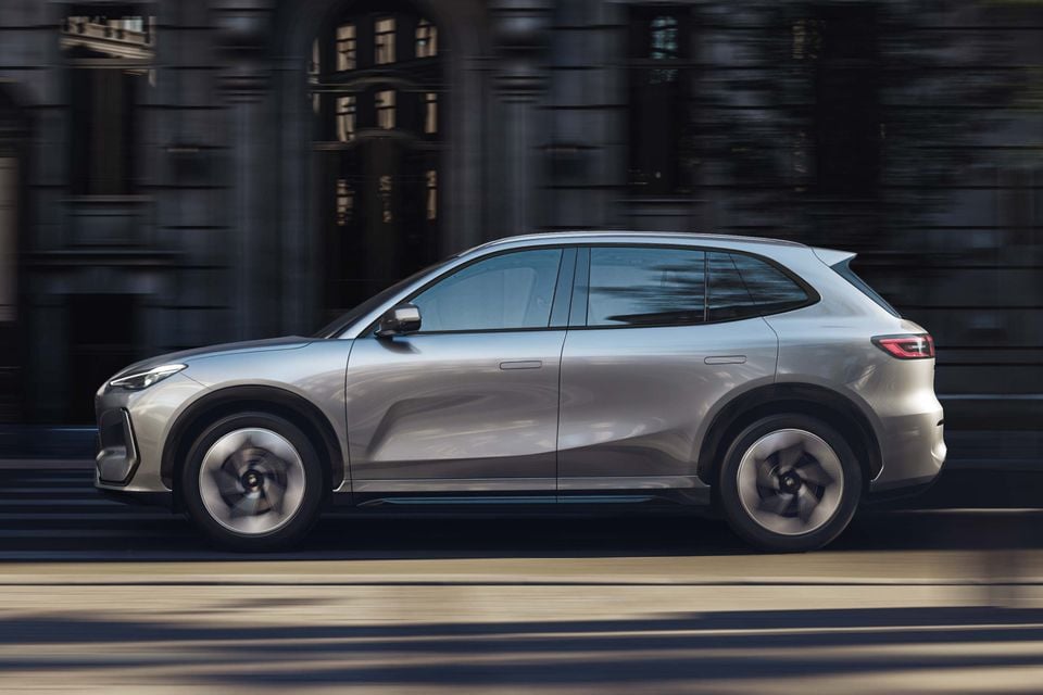 A silver Geely Galaxy E5 SUV driving along a city street, seen from the side.