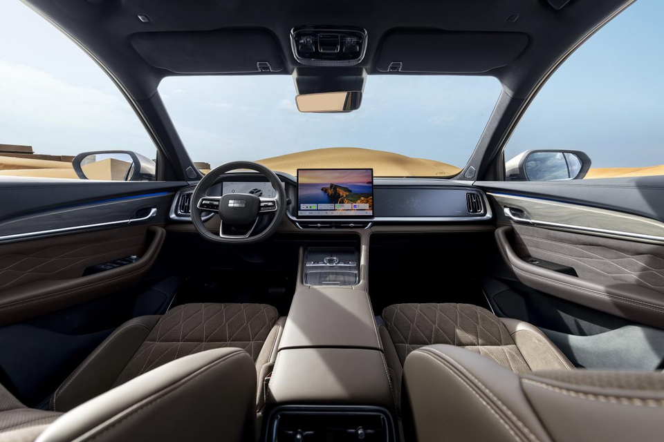 Interior of a Geely Monjaro EM-I showing the dashboard, large central touchscreen infotainment display, quilted brown and beige seats, and steering wheel, with a desert landscape visible through the windscreen.