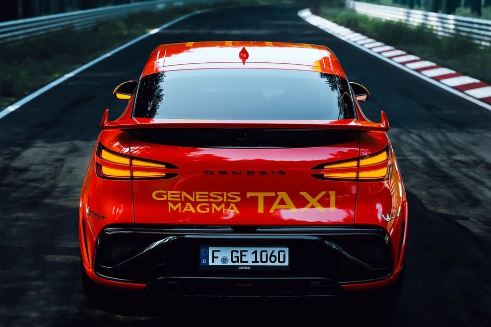 Rear view of a red Genesis GV60 Magma, badged as a 'Genesis Magma Taxi', on the Nurburgring Nordschleife circuit