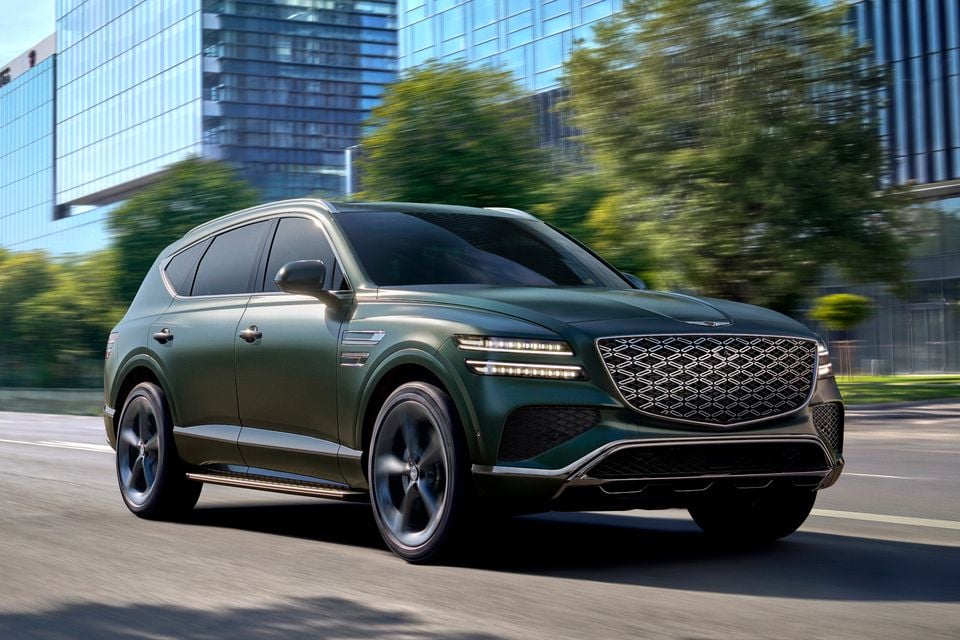 A green Genesis GV80 SUV driving on a city street, seen from the front-side angle